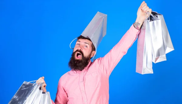 Guy magasinant sur la saison des ventes avec des réductions. Hipster sur le visage heureux avec sac sur la tête est accro au shopping. Concept de shopping. Homme à la barbe et la moustache porte des sacs à provisions, fond bleu — Photo