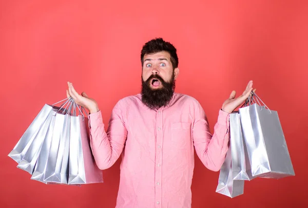 Typen, die in der Verkaufssaison mit Rabatten einkaufen. Mann mit Bart und Schnurrbart hält Einkaufstaschen, roter Hintergrund. Hipster mit geschocktem Gesicht sind einkaufsüchtig oder shopaholic. Verkaufs- und Rabattkonzept — Stockfoto