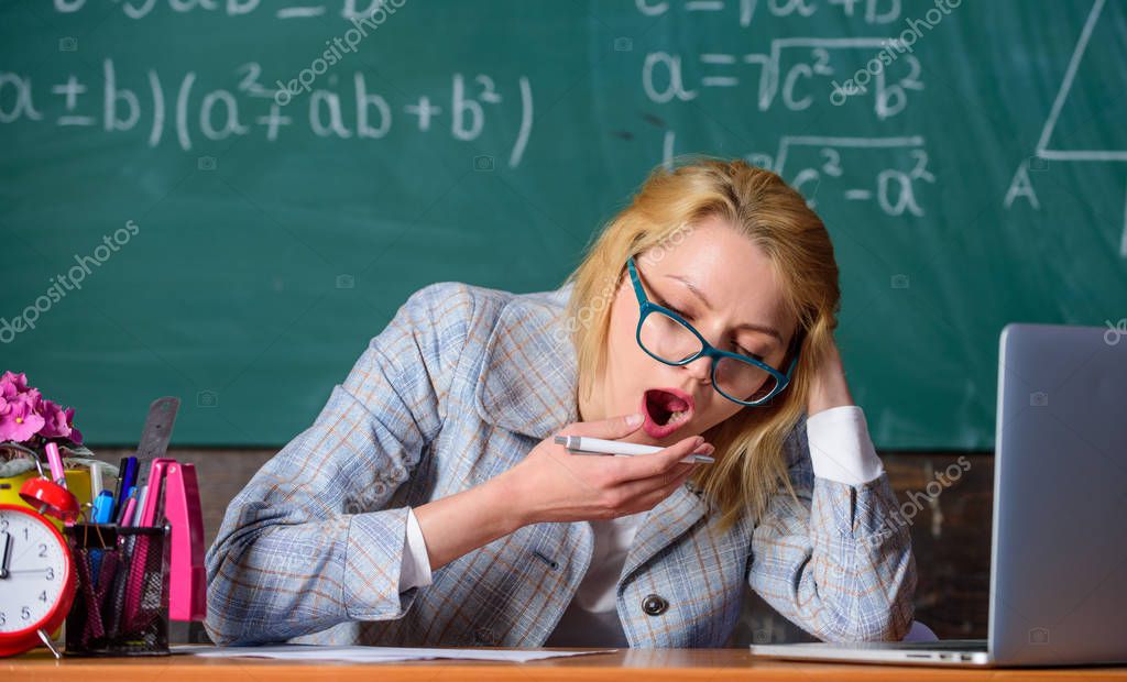 Still working. Work far beyond actual school day. Teacher woman sit table classroom chalkboard background. Teacher busy with paperwork and research. Teacher tired face keep working after classes.