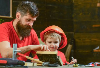 Çocuk, Çocuk koruyucu kask hobnails baba ile çekiç için öğrenme içinde meşgul. Erkeksi görevleri kavramı. Baba, sakallı hobnails ve çekiç kullanmak için küçük oğlu öğretim üst