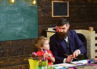 Sakallı öğretmeni, sınıfta, kara tahta arka plan çizmek için küçük oğlu baba öğretir. Sanat ders kavramı. Çocuk ve meşgul yüz boyama, resim öğretmeni. Yetenekli sanatçı oğlumla vakit geçirmek