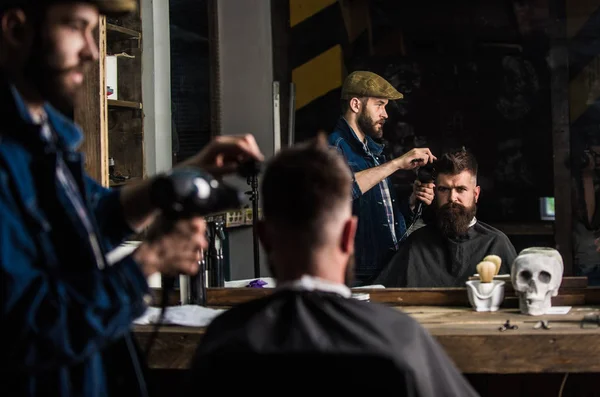 Barbeiro com secador de cabelo funciona no penteado para homem barbudo, barbearia fundo. Conceito de estilo. Barbeiro com secador de cabelo secagem e cabelo styling do cliente. Hipster barbudo cliente recebendo penteado — Fotografia de Stock