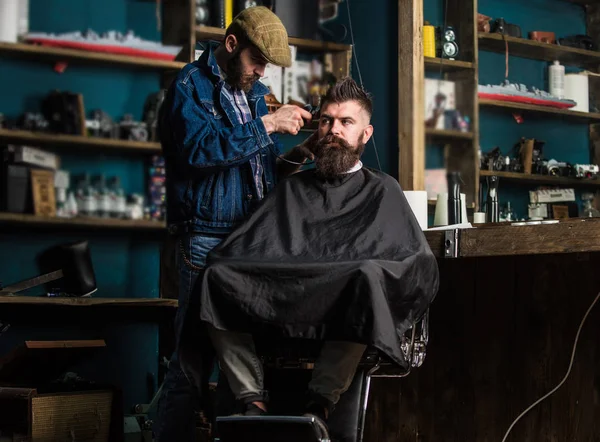 Peluquero con clipper recortar el pelo en el templo de cliente barbudo. Hipster cliente cortarse el pelo. Peluquero con cortador de pelo trabajo en el peinado para hipster, fondo de la barbería. Hipster concepto de estilo de vida — Foto de Stock