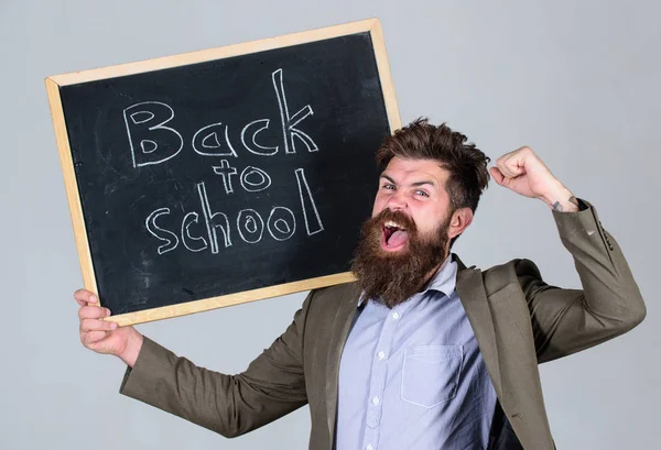 Leraar bebaarde man staat en houdt van blackboard inscriptie terug naar school grijze achtergrond. Bent u klaar om te studeren. Hiermee adverteert u leraar terug naar studeren, schooljaar beginnen. Nieuwe schooljaar voorbereiden — Stockfoto