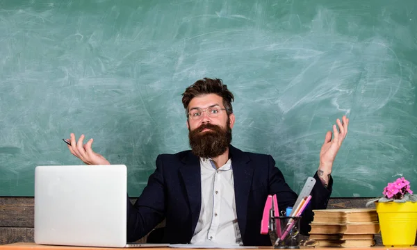 El maestro se preguntaba bajo nivel de conocimiento. Qué estúpida idea. Hombre barbudo profesor preguntándose expresión sentarse aula pizarra fondo. ¿De qué estás hablando? Maravilla desagradable —  Fotos de Stock