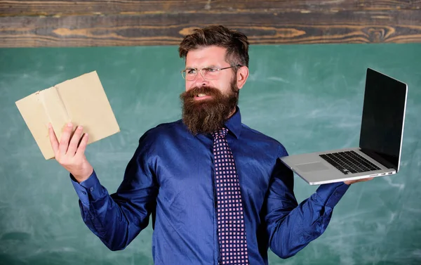 Digital contra papel. Elija el método de enseñanza correcto. Profesor eligiendo enfoque de enseñanza moderna. Profesor barbudo hipster sostiene libro y portátil. Las tecnologías modernas se benefician. Moderno en lugar anticuado —  Fotos de Stock