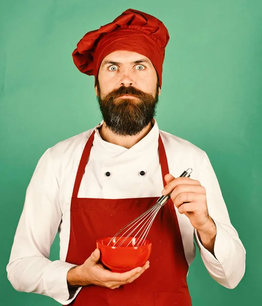 Cook with shocked face in burgundy uniform holds kitchenware — Stock Photo, Image