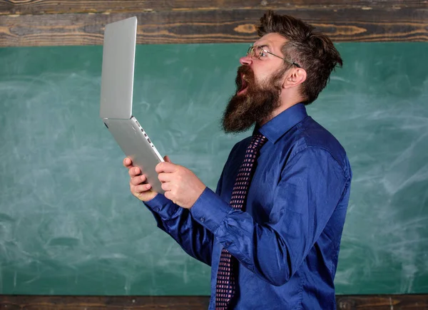 Annoyed by slow internet. Slowly internet annoying him. Hipster teacher aggressive with laptop goes mad about slow speed internet connection. Teacher bearded man modern laptop chalkboard background — Stock Photo, Image