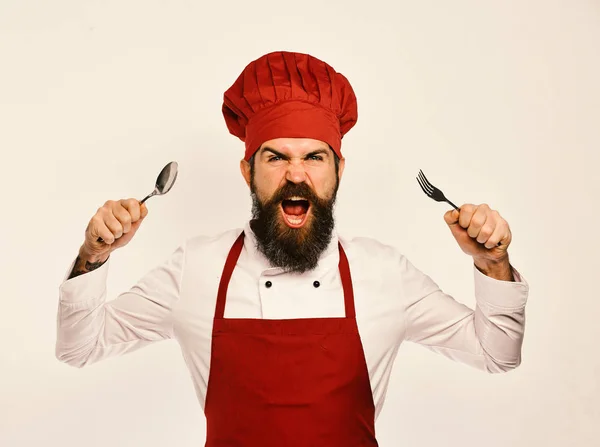 Cocinero con la cara enojada en uniforme de color burdeos muestra cubiertos — Foto de Stock