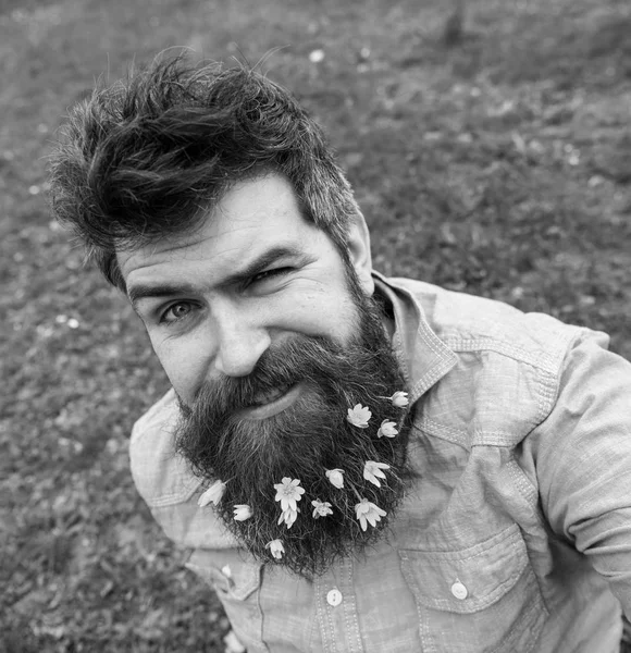 Csípő, a Kacsintó ül a fűben, defocused. Férfi szakállal élvezi a tavasz, zöld rét háttér. Tavaszi szezon koncepció. Srác Salátaboglárka virágok szakáll selfie fénykép — Stock Fotó