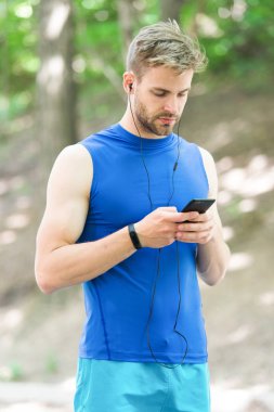 Adam atlet meşgul yüz kadar çalma listesi, Doğa arka plan ayarlayın. Adım sayar ve kulaklık becerikli alet eğitim sporcu. Atlet ile kıl fitness izci veya adım sayar. Gadget'ı yapmak hayat daha kolay