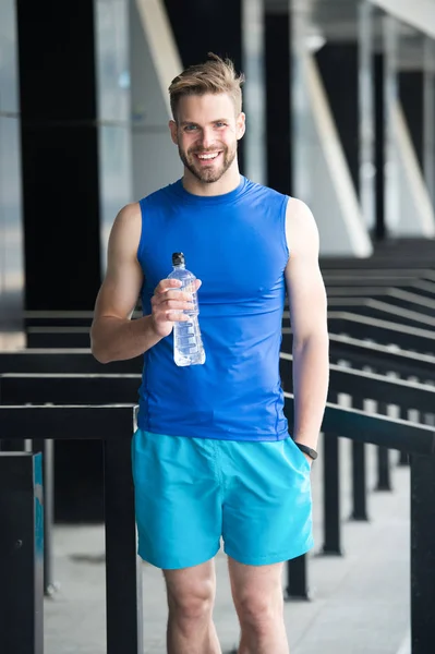 Sporty nutrition concept. Man athlete hold plastic bottle care hydration body after workout. Refreshing vitamin drink. Athlete drink water after training. Man athletic appearance holds water bottle