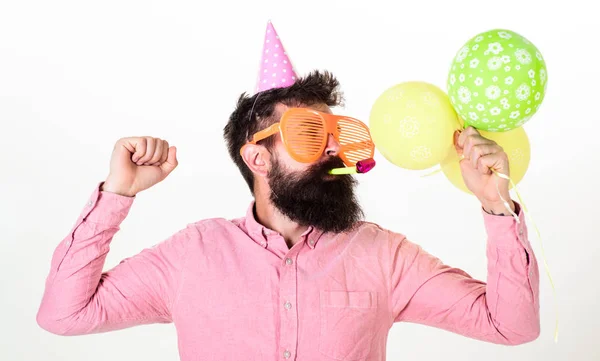 Viering concept. Guy in feest hoed met lucht ballonnen viert. Hipster in gigantische zonnebril viert verjaardag. Man met baard en snor op drukke gezicht blaast in partij hoorn, witte achtergrond — Stockfoto