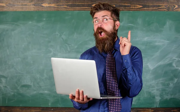 Innovación escolar. Concepto de educación a distancia. Hipster profesor usar gafas y corbata sostiene portátil navegar por Internet. Profesor barbudo hombre con portátil moderno navegar por internet pizarra fondo —  Fotos de Stock