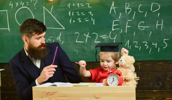 Estudante fazendo hometask com o pai e escrevendo no caderno de trabalho, quadro-negro no fundo. O pai a verificar as tarefas domésticas, ajuda o rapaz, filho. Conceito de tarefas domésticas. Criança entusiasmada estudando com professor — Fotografia de Stock