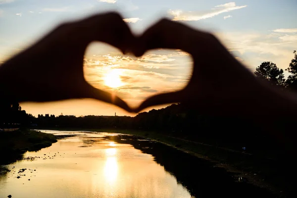 Idea honeymoon travel. Honeymoon summer resort. Romantic date ideas. Silhouette heart gesture symbol of love romance. Sunset sunlight romantic atmosphere. Heart gesture in front of sunset above river