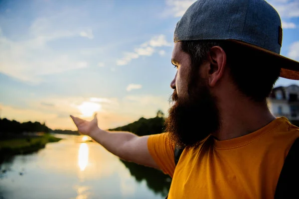 Take moment to admire sunset nature beauty. River sun reflection. Man in cap enjoy sunset while stand on bridge. Enjoy pleasant moment. Guy in front of blue sky at evening time admire landscape