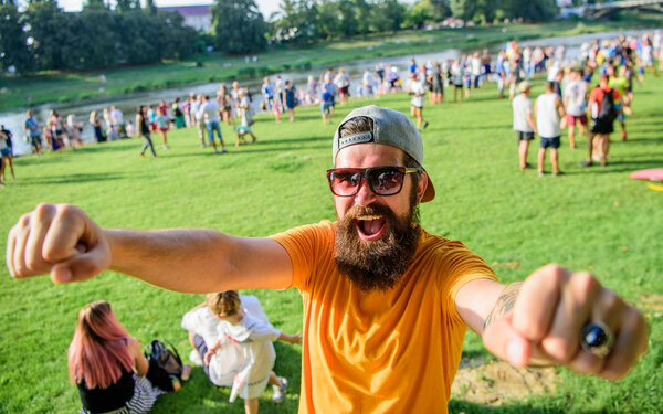 Человек бородатый хипстер перед толпой люди поднимают кулаки зеленого цвета на берегу реки. Хипстер в кепке счастливо отпраздновать событие пикник или фестиваль. Празднование городского события. Веселый болельщик на летнем фестивале
