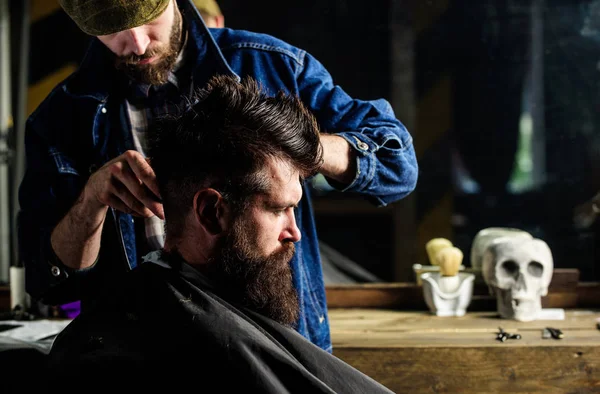 Hipster client getting haircut. Barber styling hair of brutal bearded client with clipper. Haircut concept. Barber with hair clipper works on hairstyle for man with beard, barbershop background — Stock Photo, Image