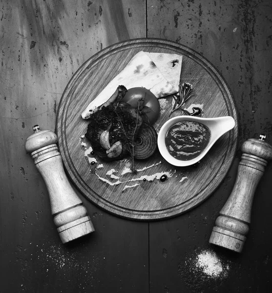 Bife assado com tomate, pão e cebola grelhada. Costelas de porco ou cordeiro com molho de churrasco em tábua de madeira — Fotografia de Stock