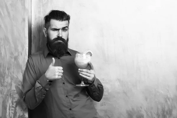 Holding tropical alcoholic fresh cocktail with orange piece on golden texture background, copy space. Brutal caucasian hipster holding tropical alcoholic fresh cocktail — Stock Photo, Image