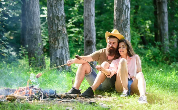 Hipster i dziewczyna pieczenie kiełbasek. Para przygotować kiełbaski pieczone przekąska tle natura. Camping i piknik. Para w lesie camping miłości, pieczenie kiełbasy. Tradycyjne potrawy pieczone piknik wycieczka — Zdjęcie stockowe