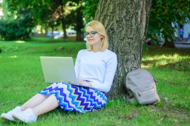 Bayan, serbest meslek sahibi Park'ta çalışma. Wi fi ağ bağlantısı ücretsiz erişim. Kadın dizüstü işleri açık, park arka plan ile. Ücretsiz wi fi avantajları alarak. Kız oturup ot yalın ağaç gövdesi ile defter