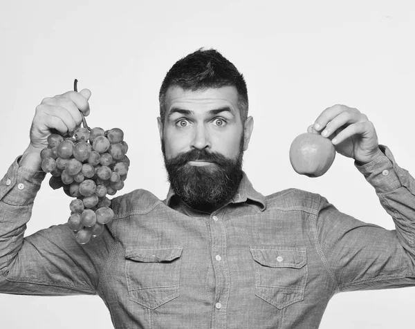 Weinbau und Gartenbaukonzept. Mann mit Bart hält Bündel grüner Trauben und Apfel in der Hand — Stockfoto