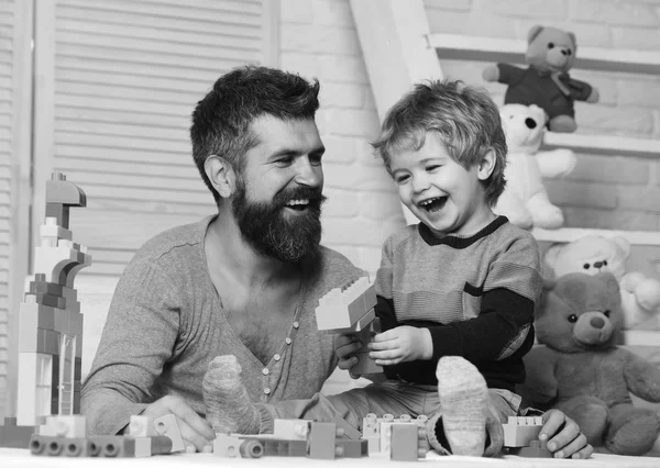 Padre e hijo con caras felices crean colorida pistola de juguete con ladrillos. Chico y hombre juegan juntos. Papá y niño con juguetes — Foto de Stock