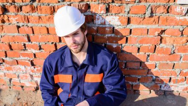 Adam koruyucu kask yakışıklı Oluşturucusu sakallı. Sakin ol bekle. İnşaat alanında ara çalışma günü çıkart. Oluşturucu kask inşaat alanında oturup rahatlatıcı yalın tuğla duvar