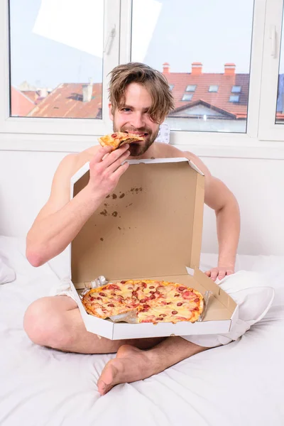 Il mange des pizzas. Guy nu couvert boîte à pizza assis lit chambre à coucher vous offrent de le rejoindre. Courrier sexy offre une satisfaction gastronomique. Satisfaction gastronomique. homme barbu beau manger pizza — Photo