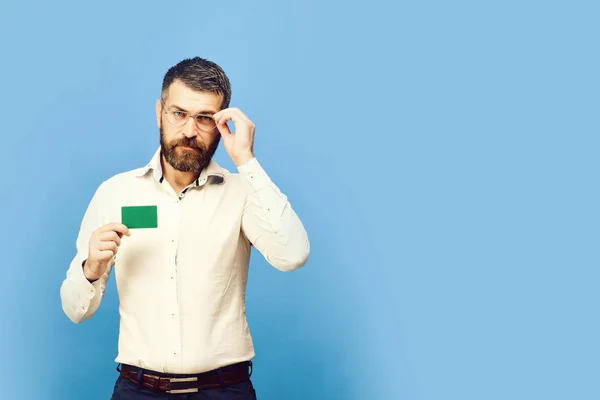 흰 셔츠에 수염을 가진 남자는 그린 비즈니스 카드를 보유 하고있다. 안경 파란색 배경에 고립 된 스마트 얼굴을 가진 남자 — 스톡 사진