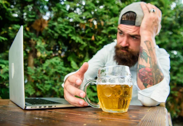 Brutal man leisure with beer and sport game. Football fan bearded hipster watch game on laptop screen. Fan watch stream online while sit terrace outdoors drink beer Disappointed with game result