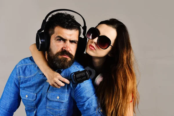 Pareja enamorada lleva auriculares y sostiene el micrófono. Hombre con barba y abrazo de niña sobre fondo gris . — Foto de Stock