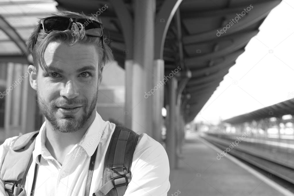 Tourist with smiling face and backpack, copy space. Missed train and travelling concept. Young man standing on platform