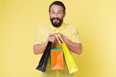 Presents make life more interesting. Man mature bearded cheerful face holds shopping bags. Man got unexpectable gifts. Guy touched by attention and gifts for him yellow background. Sincere emotions clipart