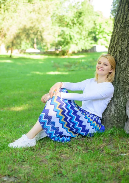Find peaceful place in park. Give yourself break and enjoy leisure. Girl sit on grass lean on tree trunk relaxing in shadow green nature background. Woman blonde take break relaxing in park