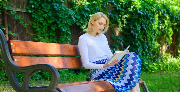女金发女郎在公园看书时休息放松。阅读文学作为爱好。最喜欢的书。女孩坐板凳放松与书, 绿色自然背景。喜欢看书的女孩 — 图库照片