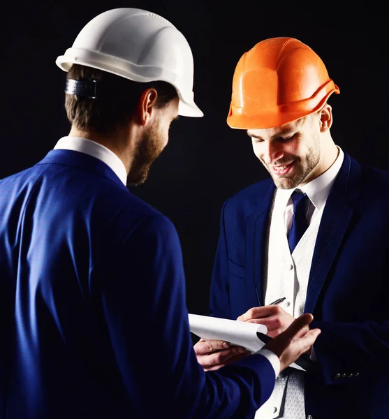 Construction, architecture, work, job concept. Engineers with smiling faces discuss project. Businessman and happy architect with architectural project. Boss in helmet gives instructions to employee