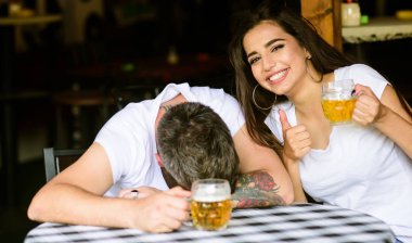Enough for him. Best friends or lover drink beer in pub. Couple in love on date drinks beer. She knows tricks how to drink and stay sober. Man drunk fall asleep on table and girl with full beer glass clipart