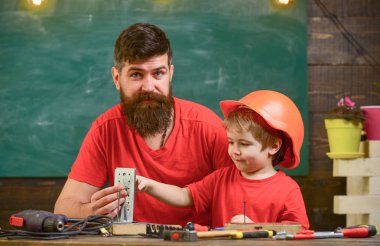 Sınıfta, arka plan kara tahta araçlarını kullanmak için küçük oğlu öğretim sakallı baba. Küçük Yardımcısı kavramı. Evlat, Çocuk koruyucu kask meşgul el ile baba ile onarım yapar