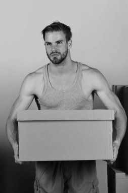 Karton kutuların arasında duran ve elinde bir tane tutan bir adam.