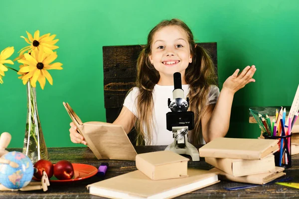 Menina com rosto alegre contém livro. Estudante senta-se na mesa — Fotografia de Stock