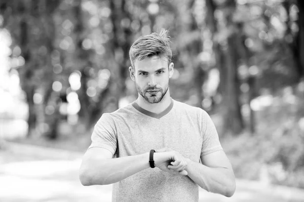 Man athlete on strict face setting up fitness tracker, nature background. Athlete with bristle with fitness tracker or pedometer. Sportsman training with pedometer gadget. Sport gadget concept