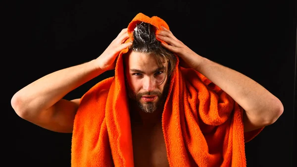 Macho ελκυστική γυμνό άντρα μαύρο φόντο. Ο άνθρωπος γένια tousled μαλλιά καλύπτεται με αφρό ή σαπούνι σαπουνάδα. Πλύντε προσεκτικά τον αφρό με νερό. Άνθρωπος με πορτοκαλί πετσέτα έτοιμο να λάβει ντους. Το νερό είναι πάνω από — Φωτογραφία Αρχείου
