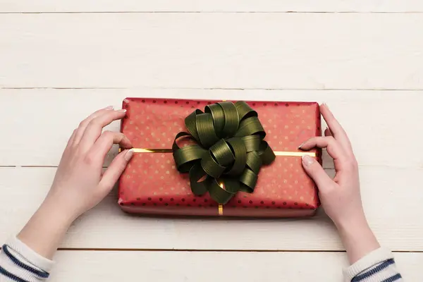 Vrouwelijke handen houd doos verpakt in rood papier met strik. — Stockfoto