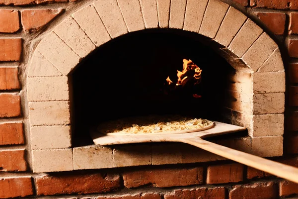 Pizza with cheese being put into oldfashioned open fire oven — Stock Photo, Image
