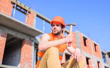 Oluşturucu yelek ve kask inşaat site sit rahatlatıcı. Adam koruyucu kask sit tuğla dışında yapılan binanın önünde. Adam çekiç inşaat alanında ara çalışma günümü alır. Rahatlamak için dakika sürer