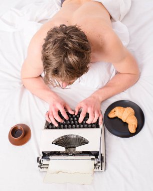 Yazar yazar eski moda daktilo kullanılan. Adam daktilo ve kahve yatıyordu yatak. Yazar adam tousled saç meşgul yazma bölüm son tarih önümüzdeki üstten görünüm. Adam yatıyordu yatak örtüsü çalışma kitabı ilham