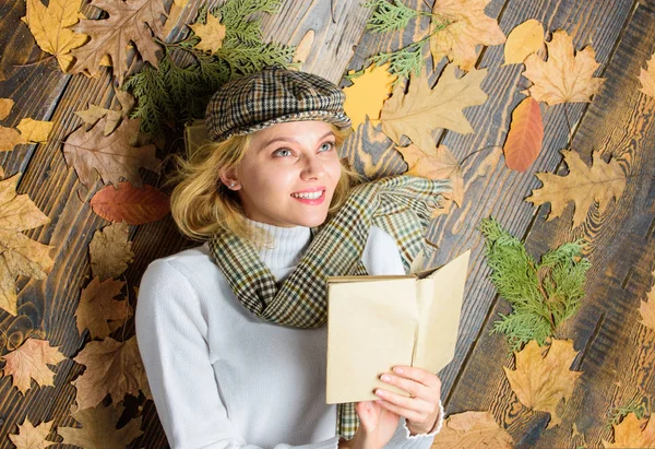Woman lady in checkered hat and scarf read book. Girl in vintage outfit enjoy literature. What to read in autumn book list. Girl blonde lay wooden background with leaves. She likes detective genre